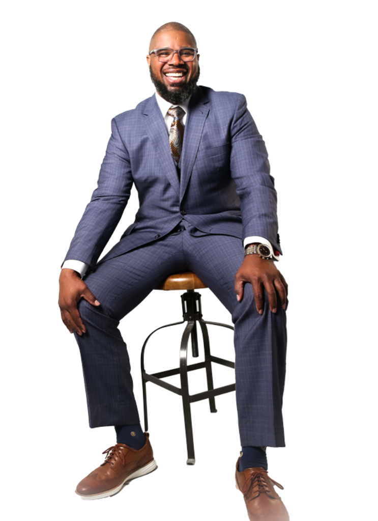 Man in a blue suit sitting on a stool, smiling confidently.