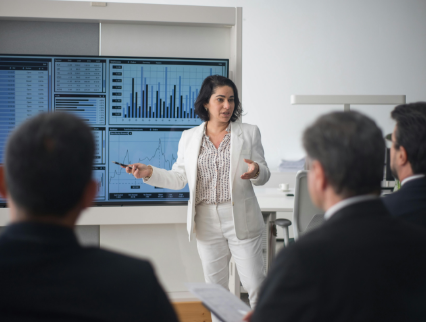 Woman in white suit presenting data charts to a group in a meeting.